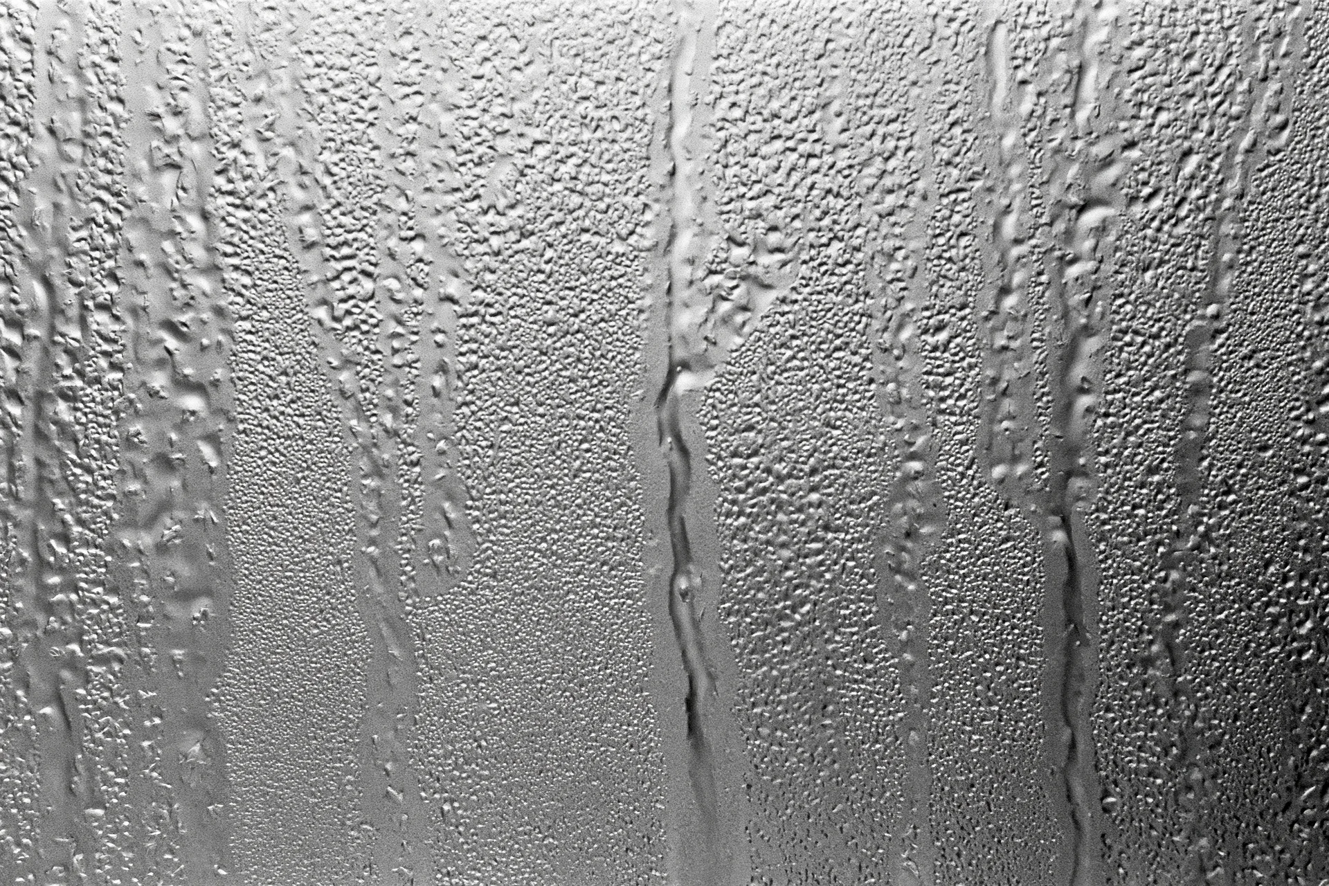 Close-up of water droplets and streaks on a fogged glass window surface
