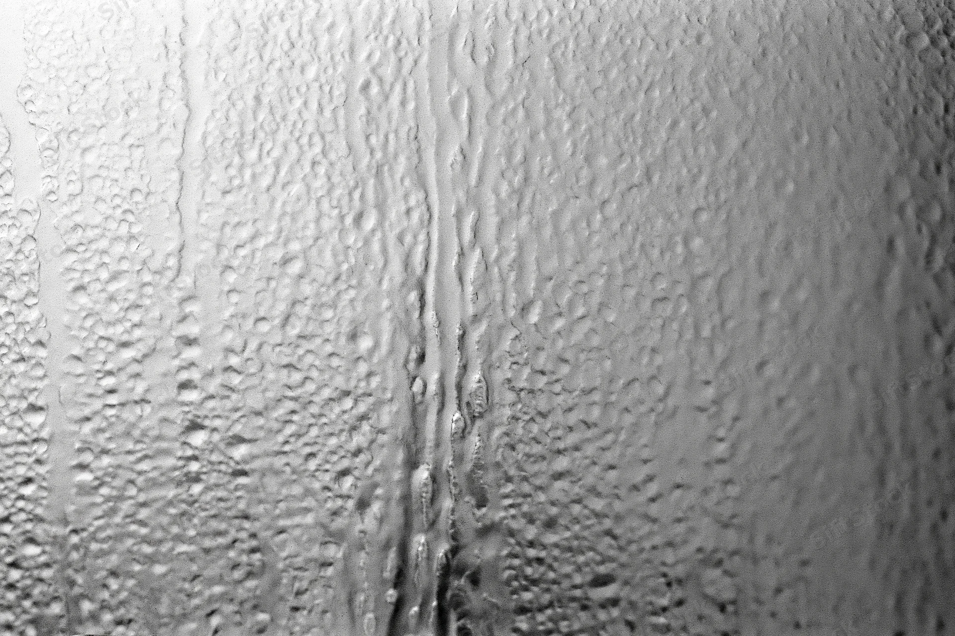 Close-up of condensation droplets and streaks on a fogged window glass surface