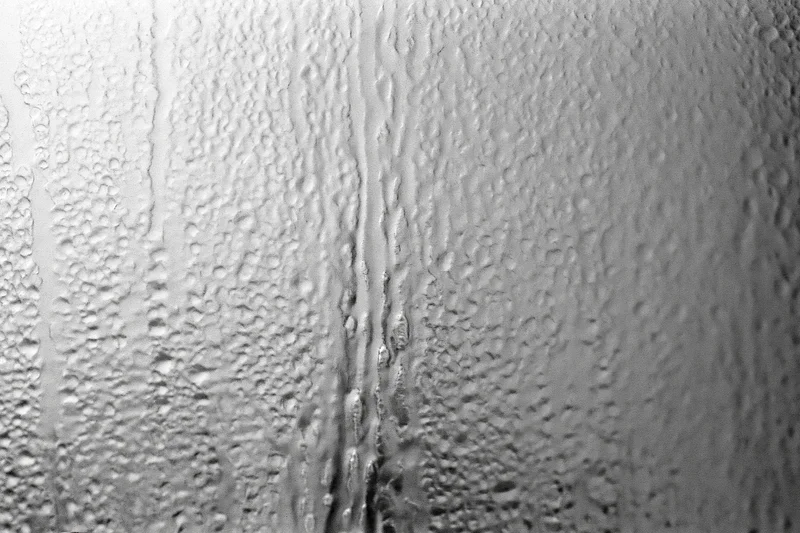 Close-up of condensation droplets and streaks on a fogged window glass surface
