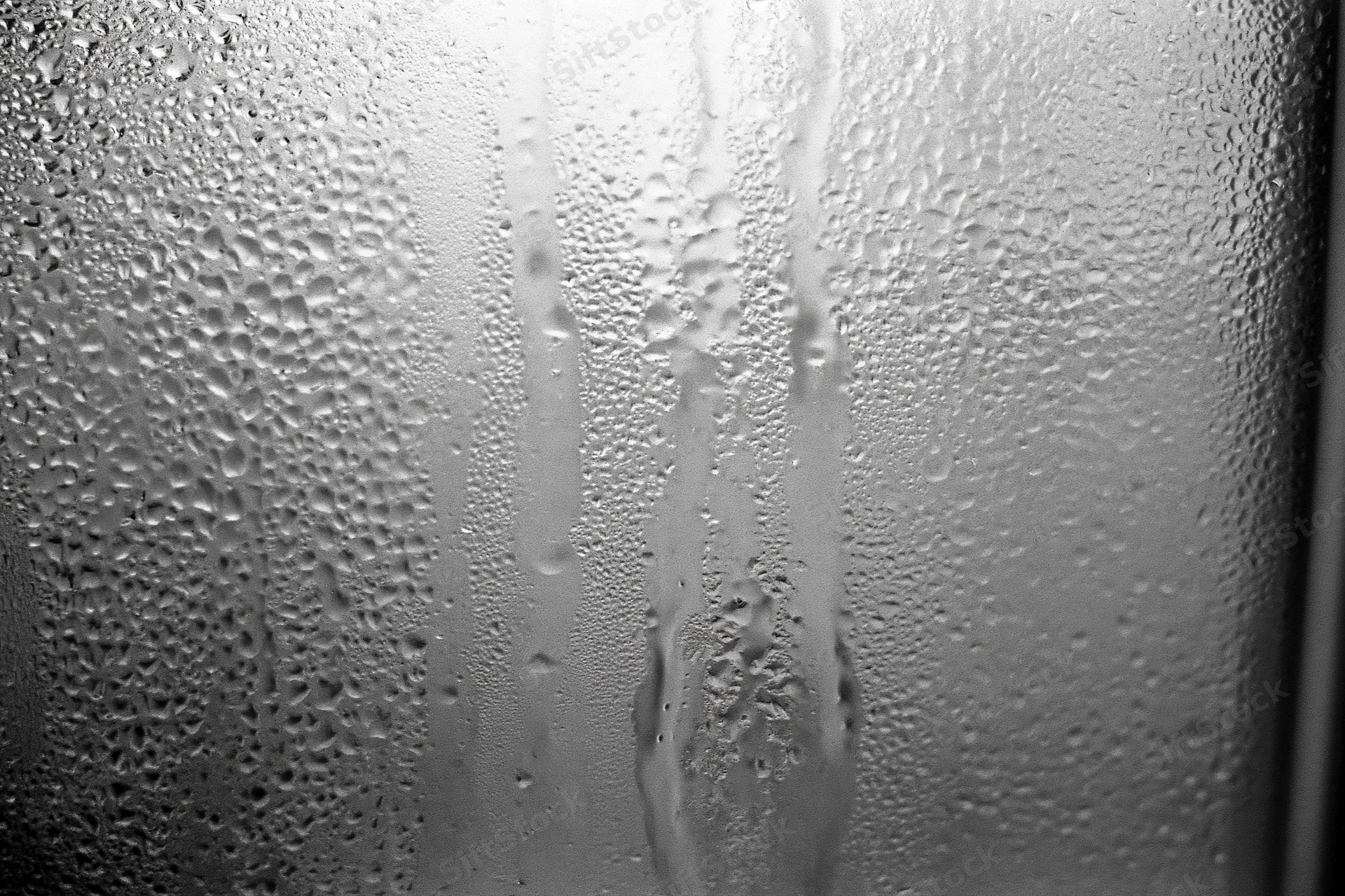Close-up of condensation droplets and streaks on a fogged window glass surface