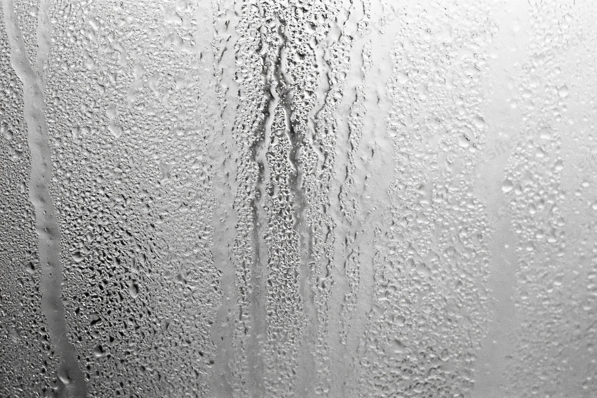 Close-up of condensation droplets and streaks on a fogged window glass surface