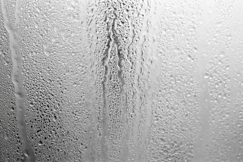 Close-up of condensation droplets and streaks on a fogged window glass surface