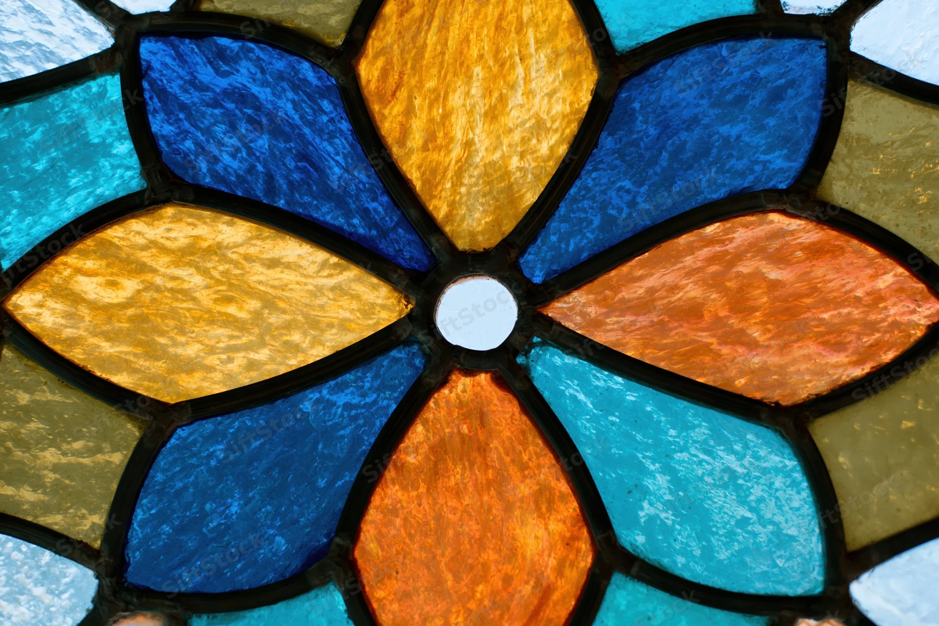 Close-up of a stained glass window with a radial floral pattern in blue, orange, yellow and teal glass segments