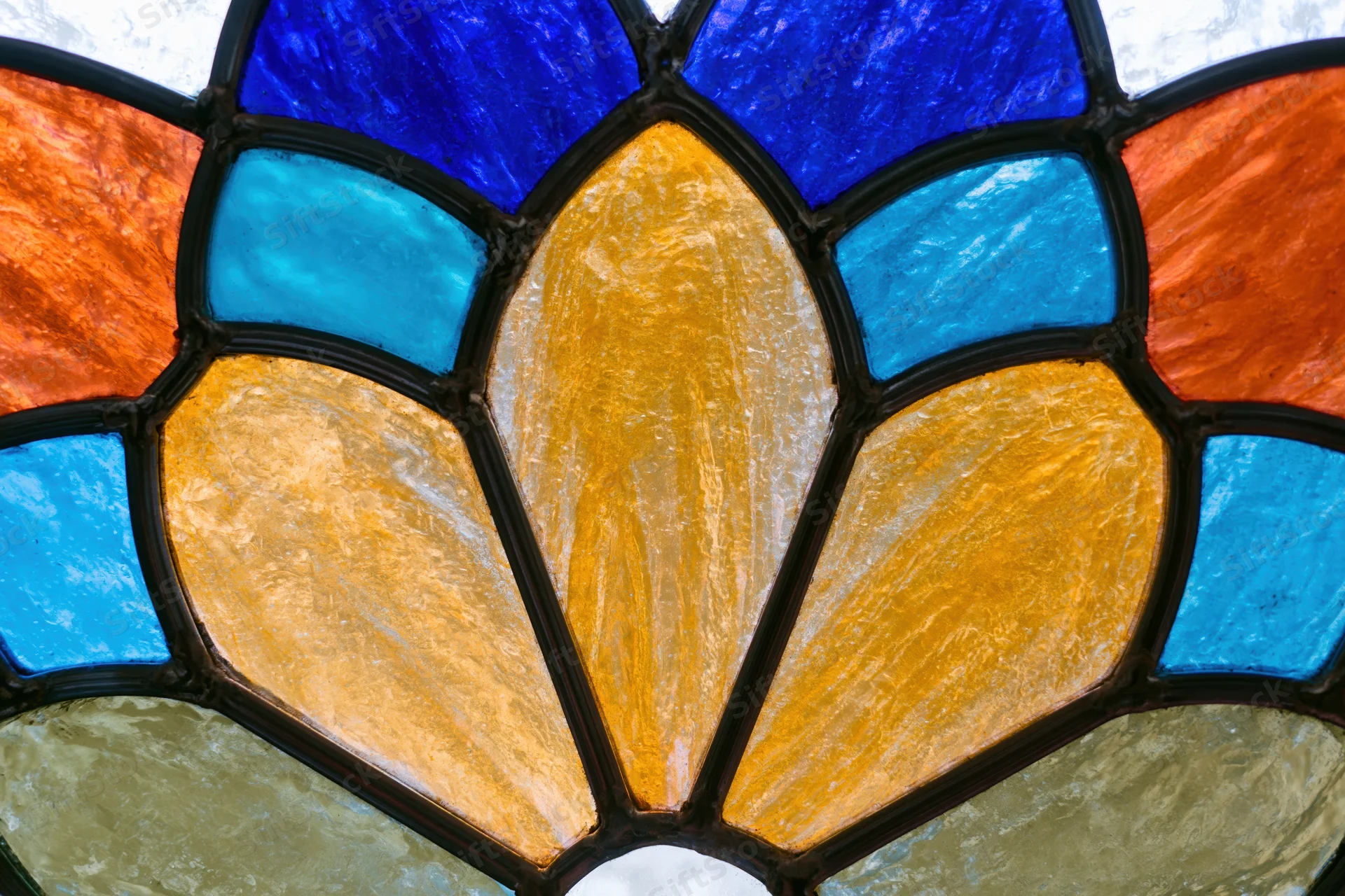 Close-up of a stained glass window with a radial pattern in blue, orange, yellow and teal glass segments