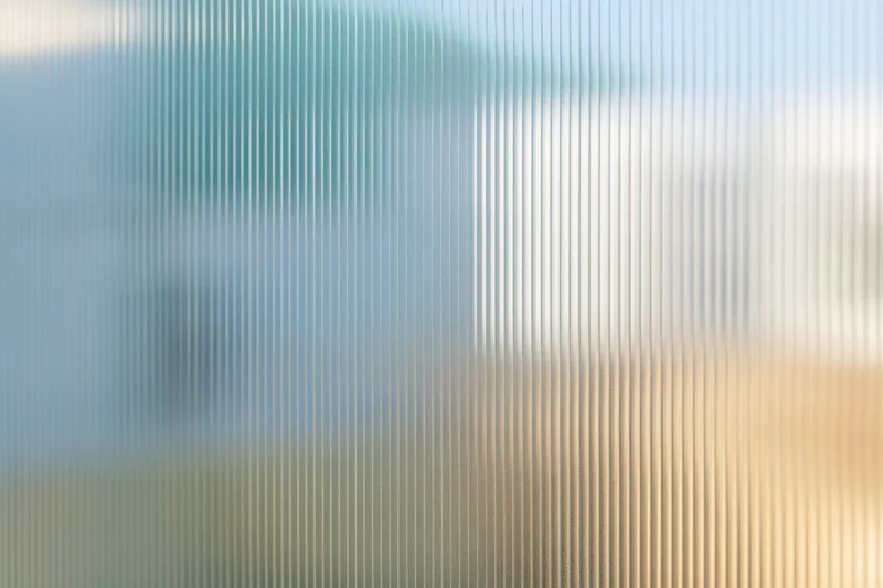 Close-up of ribbed translucent glass panel with vertical lines and diffused light, showing texture and pattern as a modern interior surface