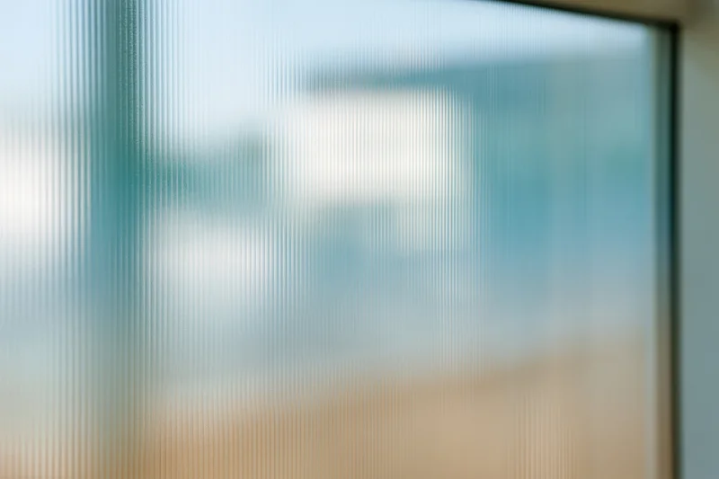 Close-up of ribbed translucent glass panel with vertical lines and diffused light, framed edge visible