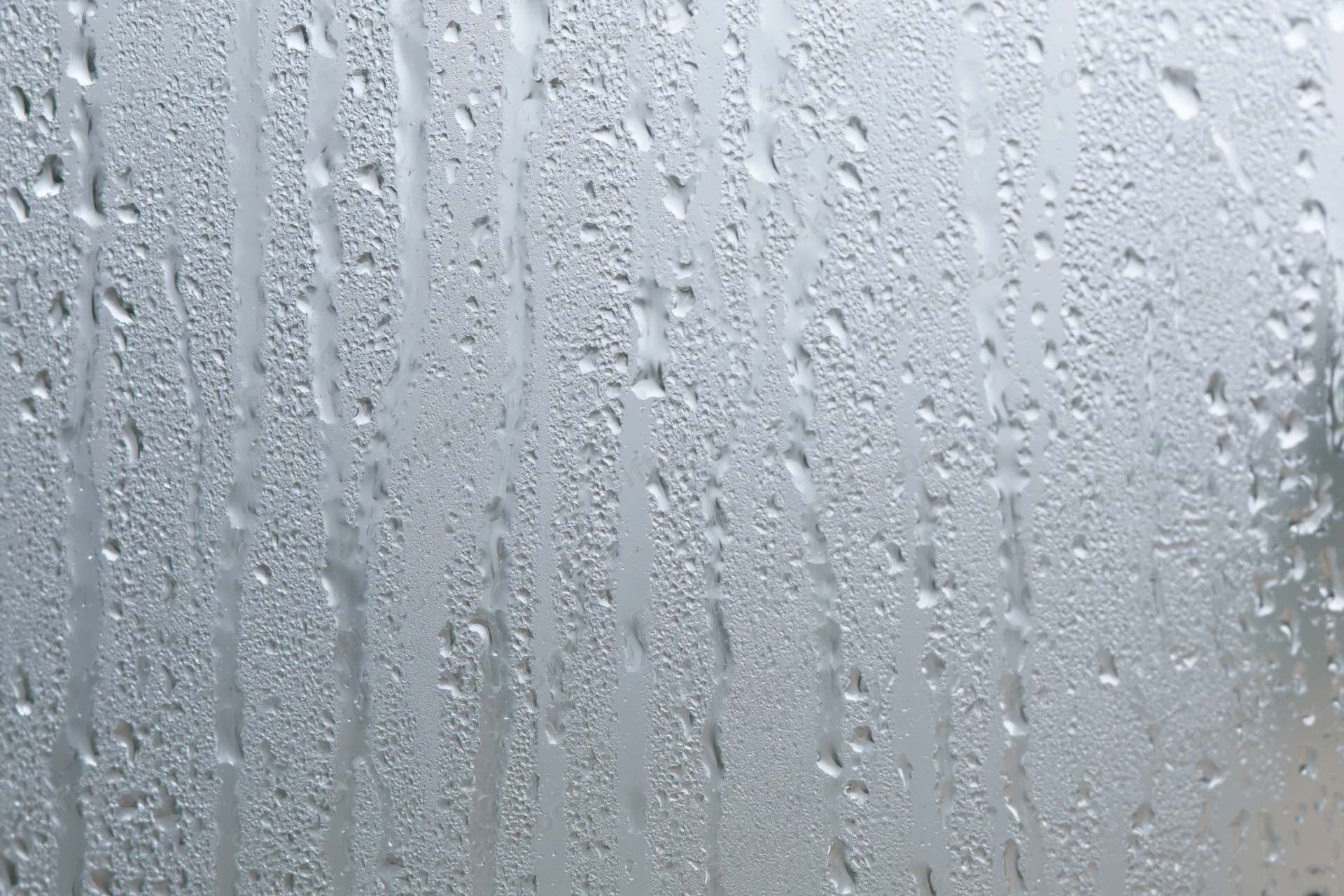 Close-up of raindrops and condensation streaks on a wet glass surface