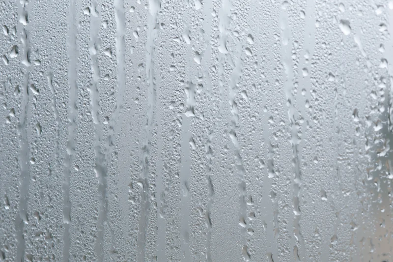 Close-up of raindrops and condensation streaks on a wet glass surface
