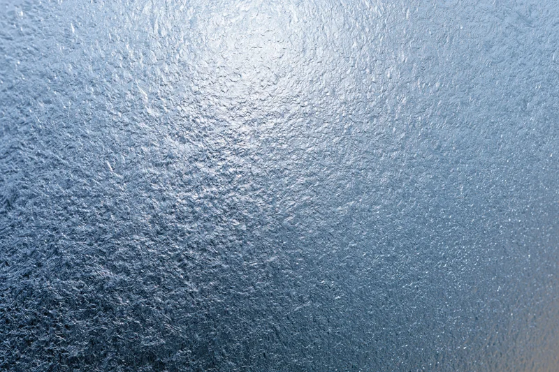 Close-up of frosted glass surface with icy texture and blue gradient