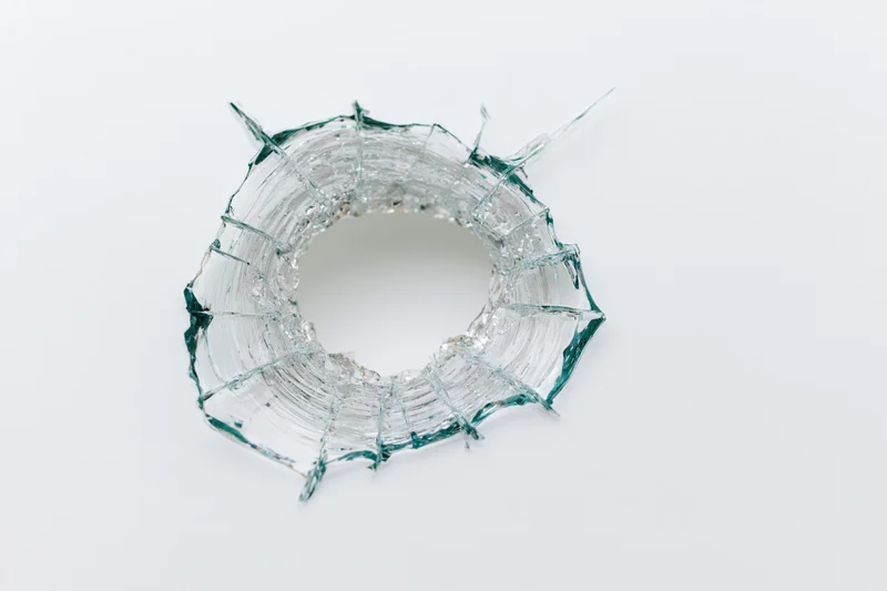 Circular bullet hole in shattered clear glass pane on white background
