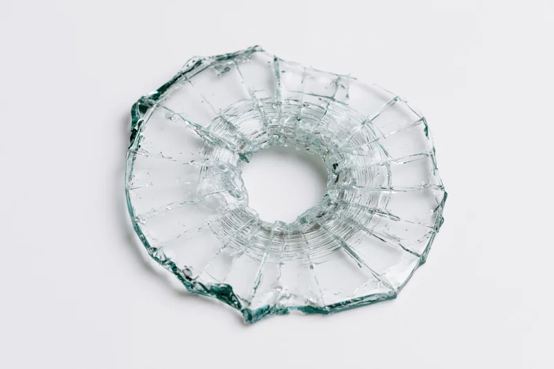 Shattered glass with circular bullet hole on white background