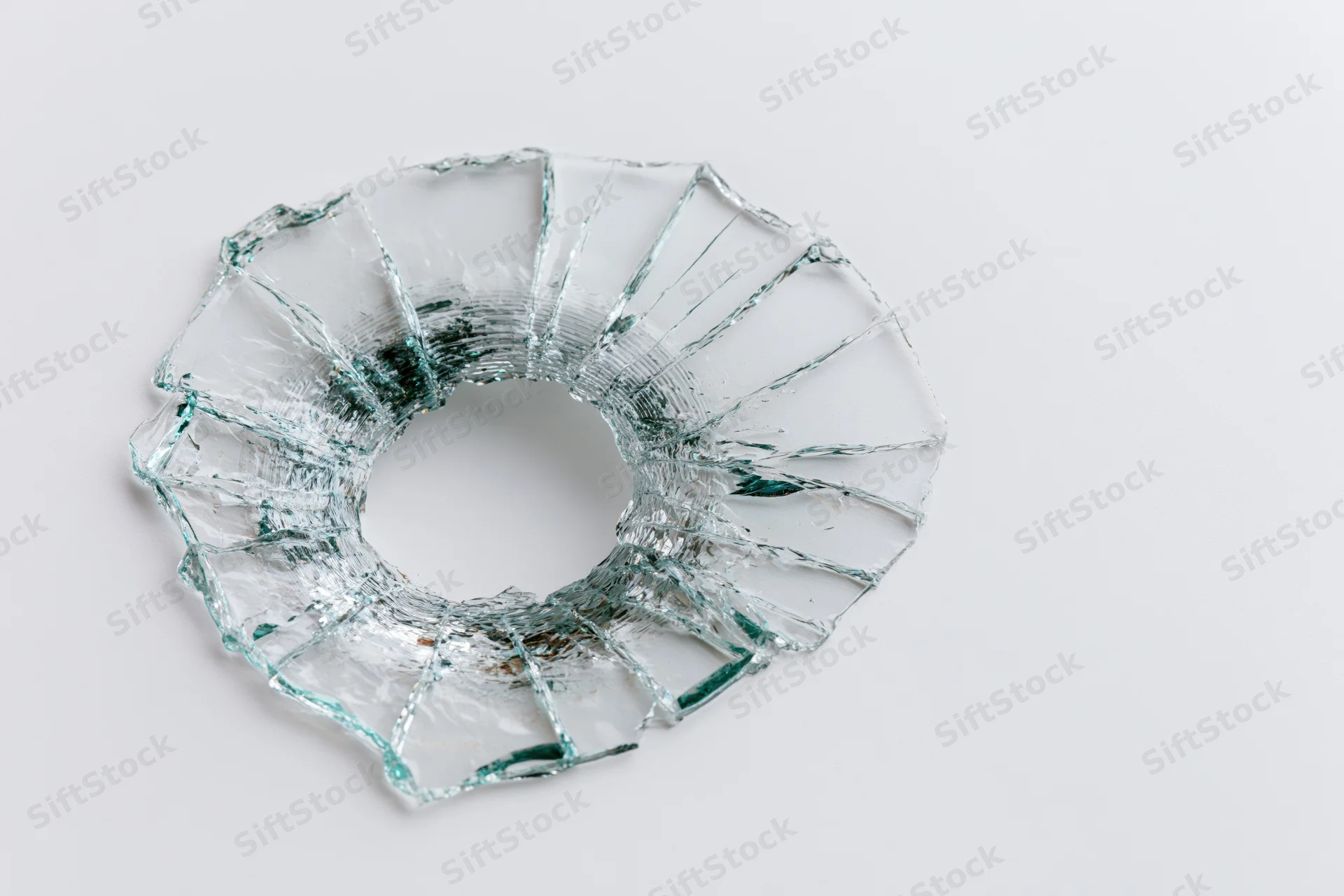 Circular bullet hole in shattered glass on white background