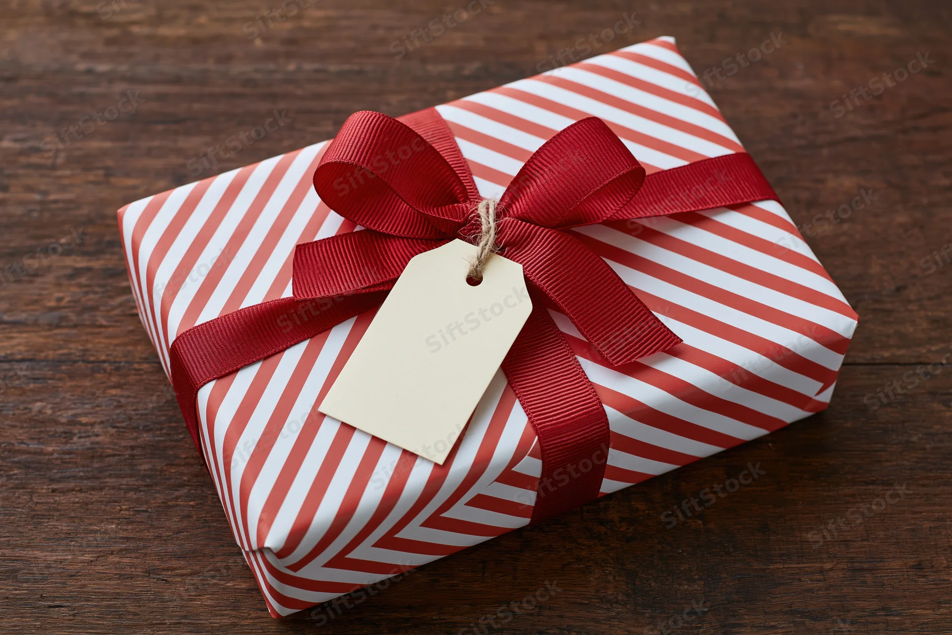 Wrapped gift box with red ribbon and blank tag on wooden surface