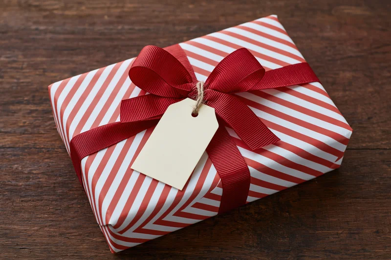 Wrapped gift box with red ribbon and blank tag on wooden surface