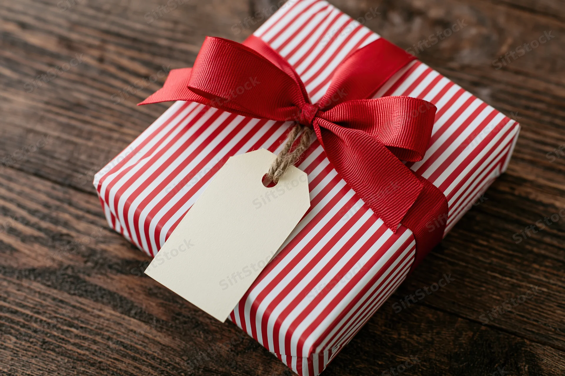 Red and white striped gift box wrapped with red ribbon and tag on wooden surface