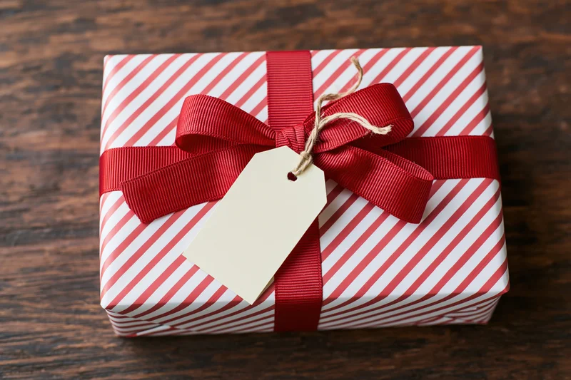 Wrapped gift box with red ribbon and blank tag on wooden surface