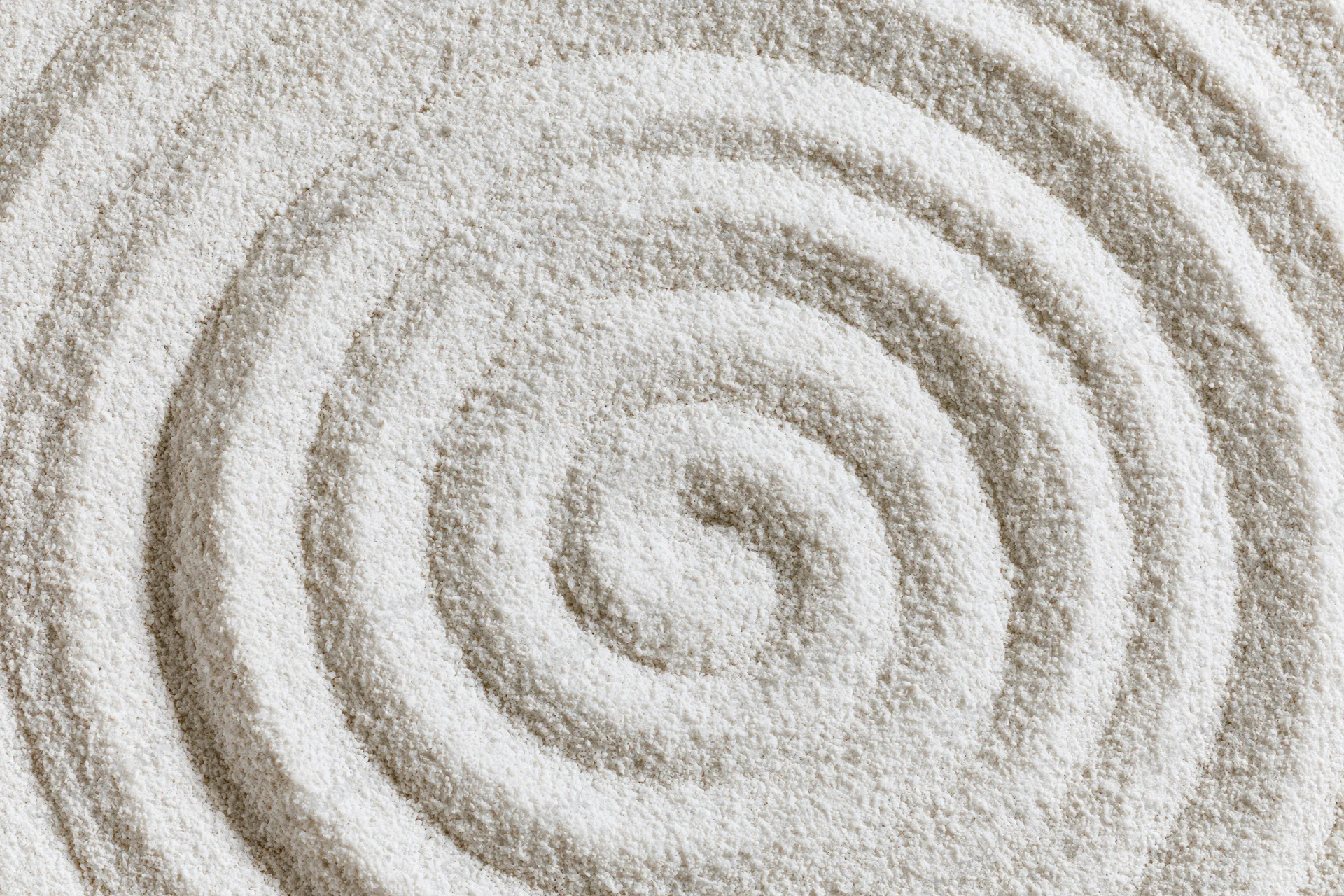 Raked spiral pattern in white sand forming concentric circles in a zen garden