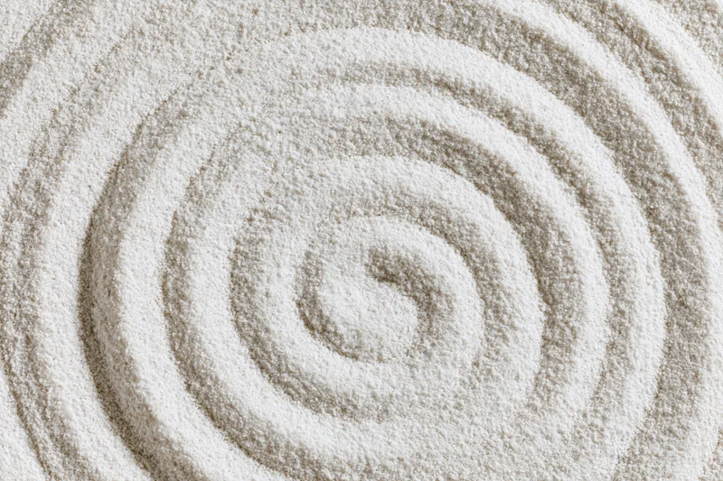 Raked spiral pattern in white sand forming concentric circles in a zen garden
