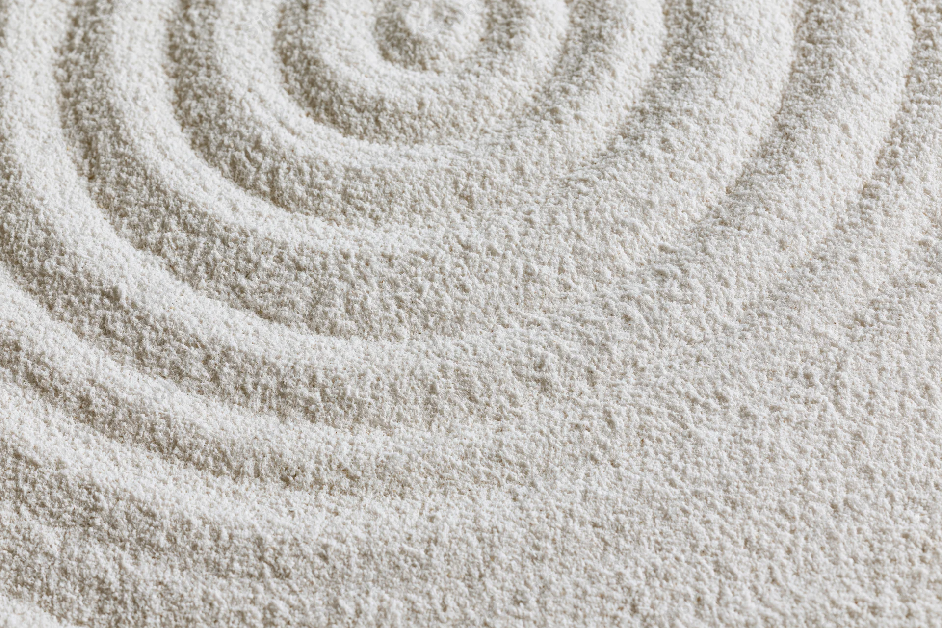 Raked white sand forming concentric spiral pattern in zen garden