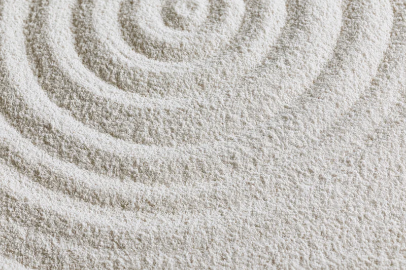 Raked white sand forming concentric spiral pattern in zen garden