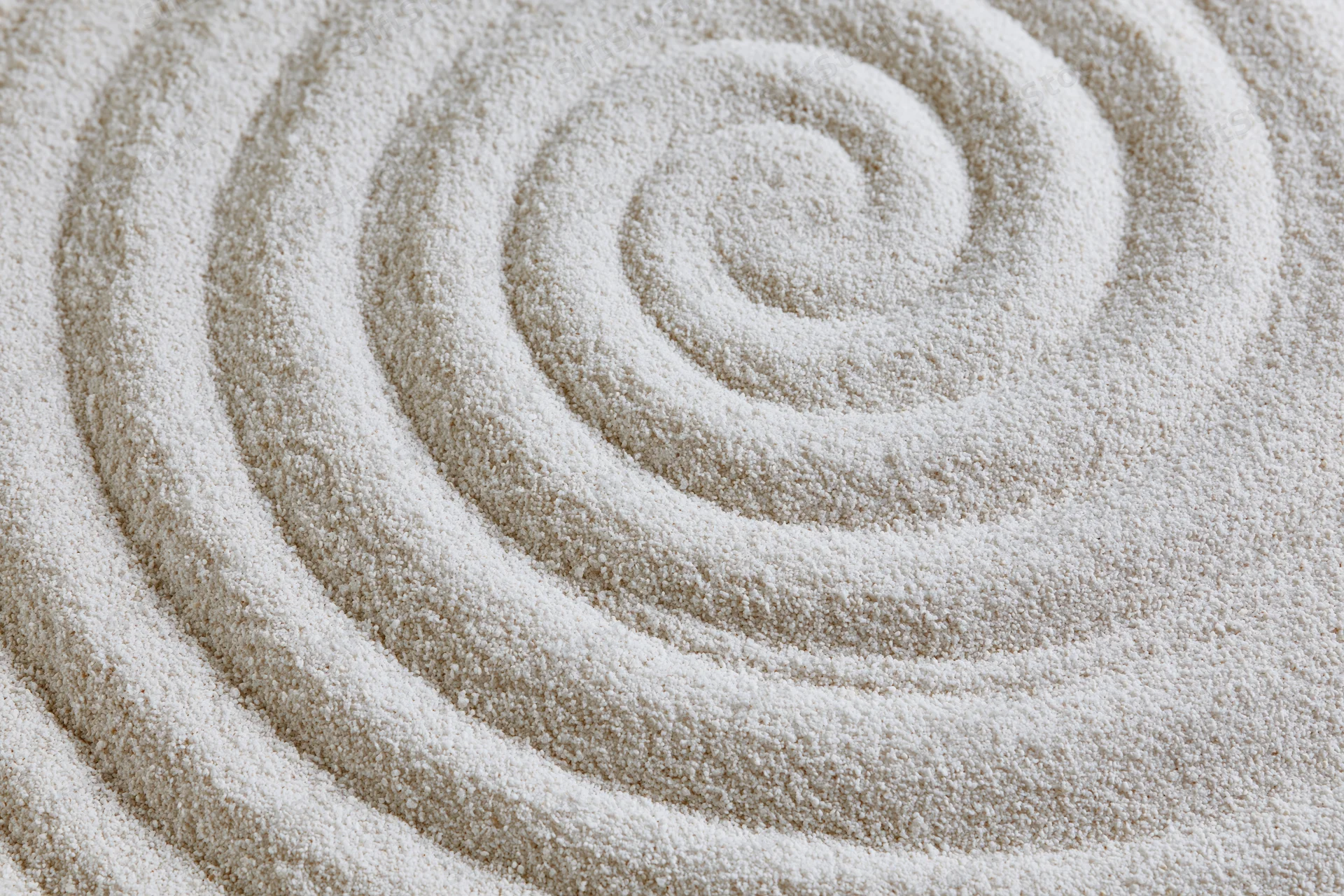 Raked white sand forming concentric spiral pattern in zen garden