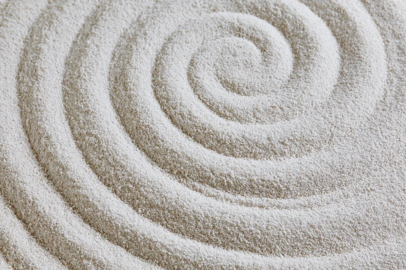 Raked white sand forming concentric spiral pattern in zen garden