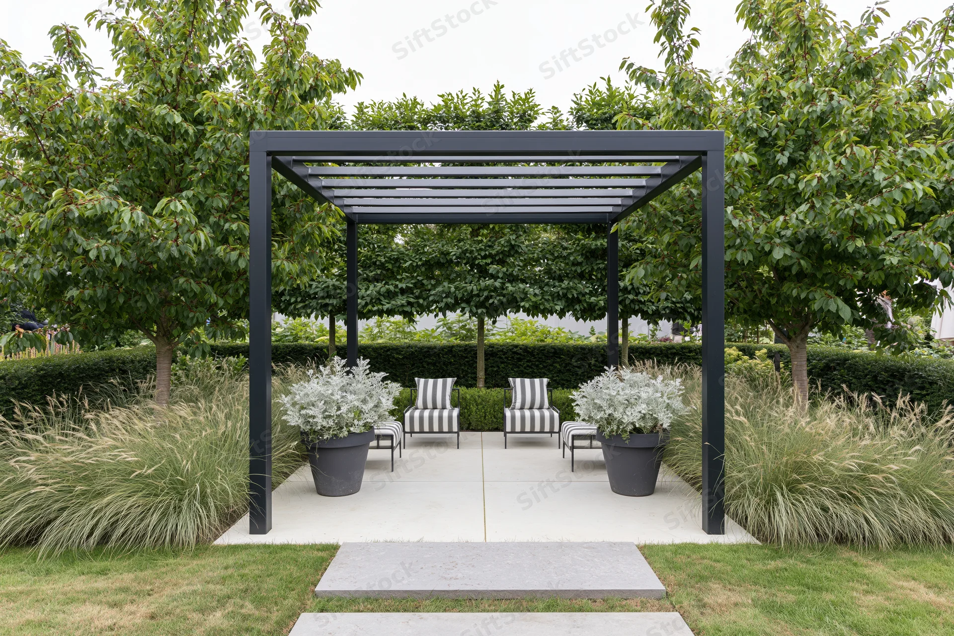 Black steel pergola over striped chairs and potted plants on a concrete patio surrounded by greenery