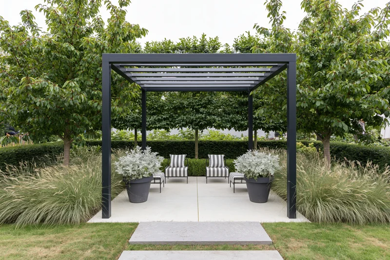 Black steel pergola over striped chairs and potted plants on a concrete patio surrounded by greenery