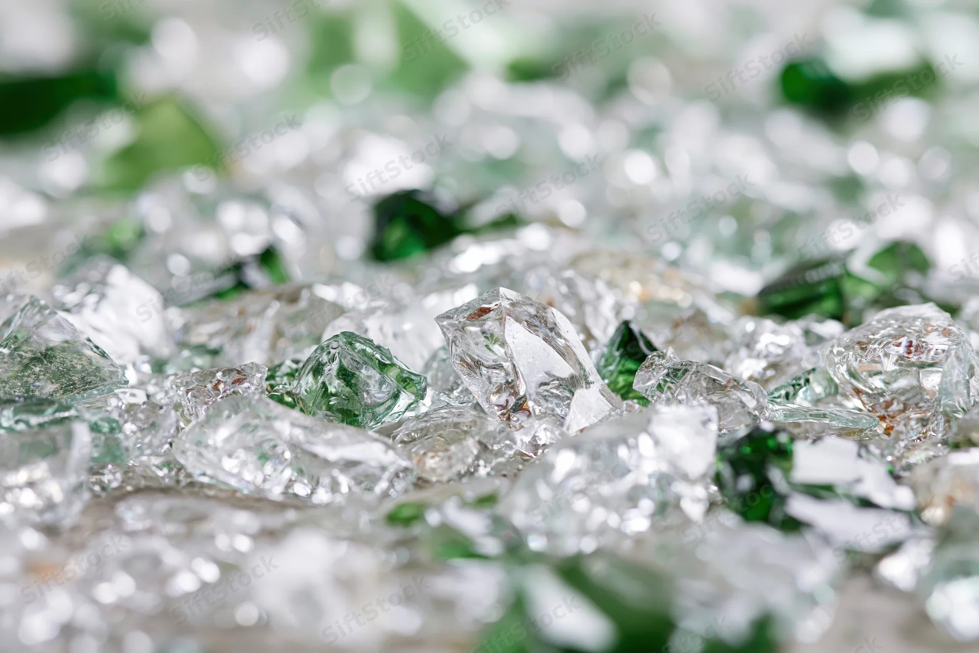 Closeup of broken glass shards scattered densely with green and clear fragments in focus