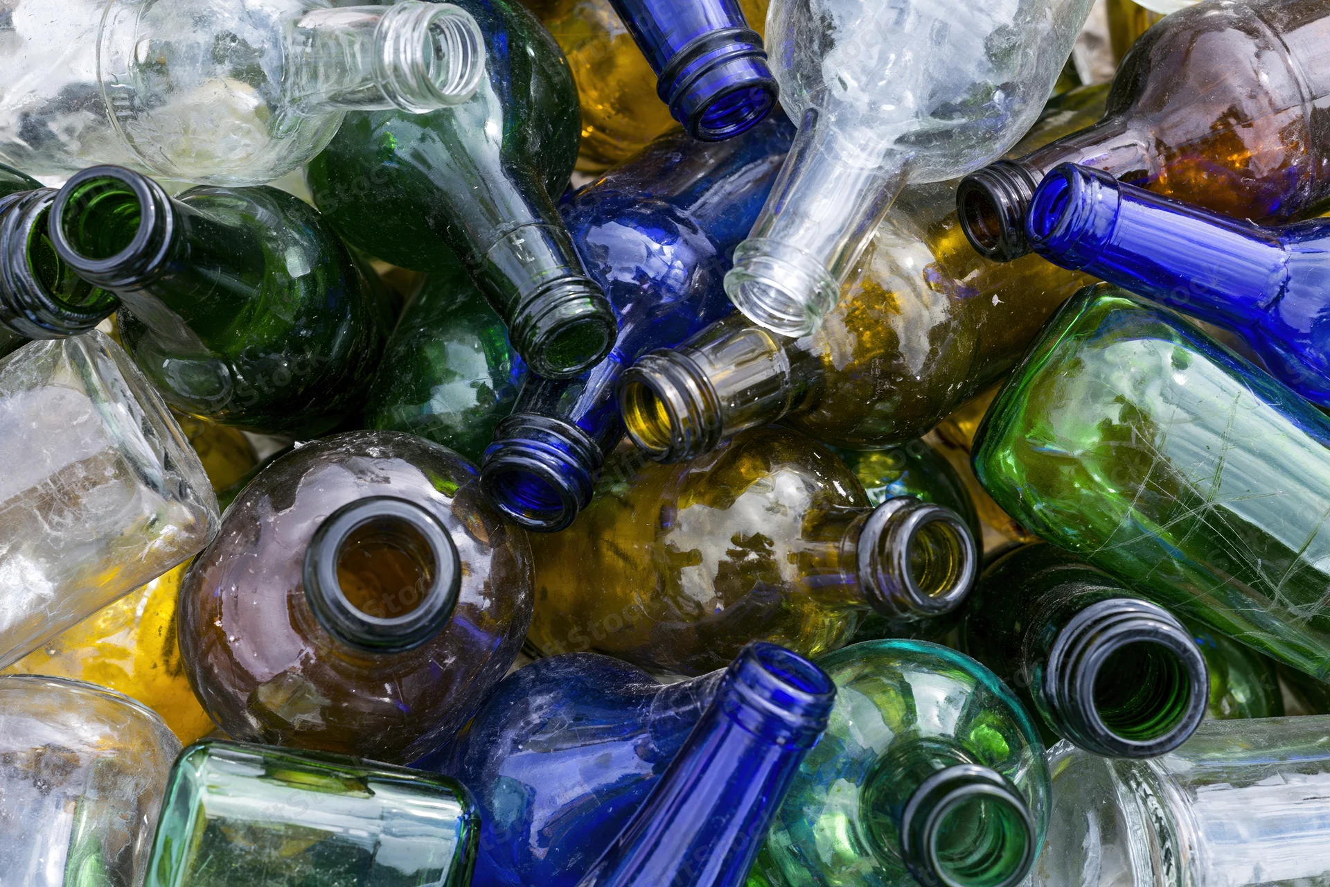 Empty glass bottles of various colors and shapes piled together in a recycling collection