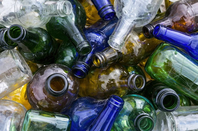 Empty glass bottles of various colors and shapes piled together in a recycling collection