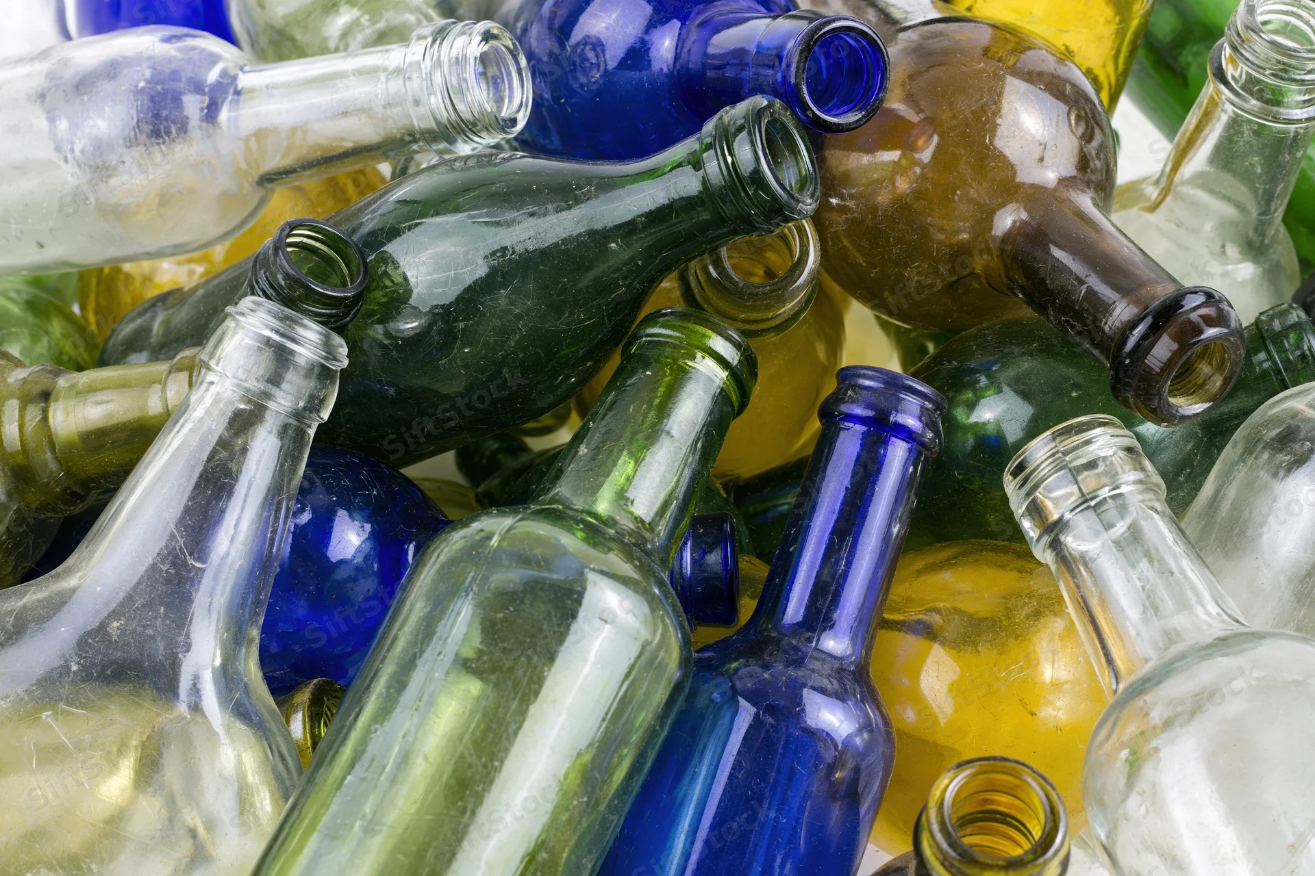 Empty glass bottles of various colors and shapes piled together in a recycling collection
