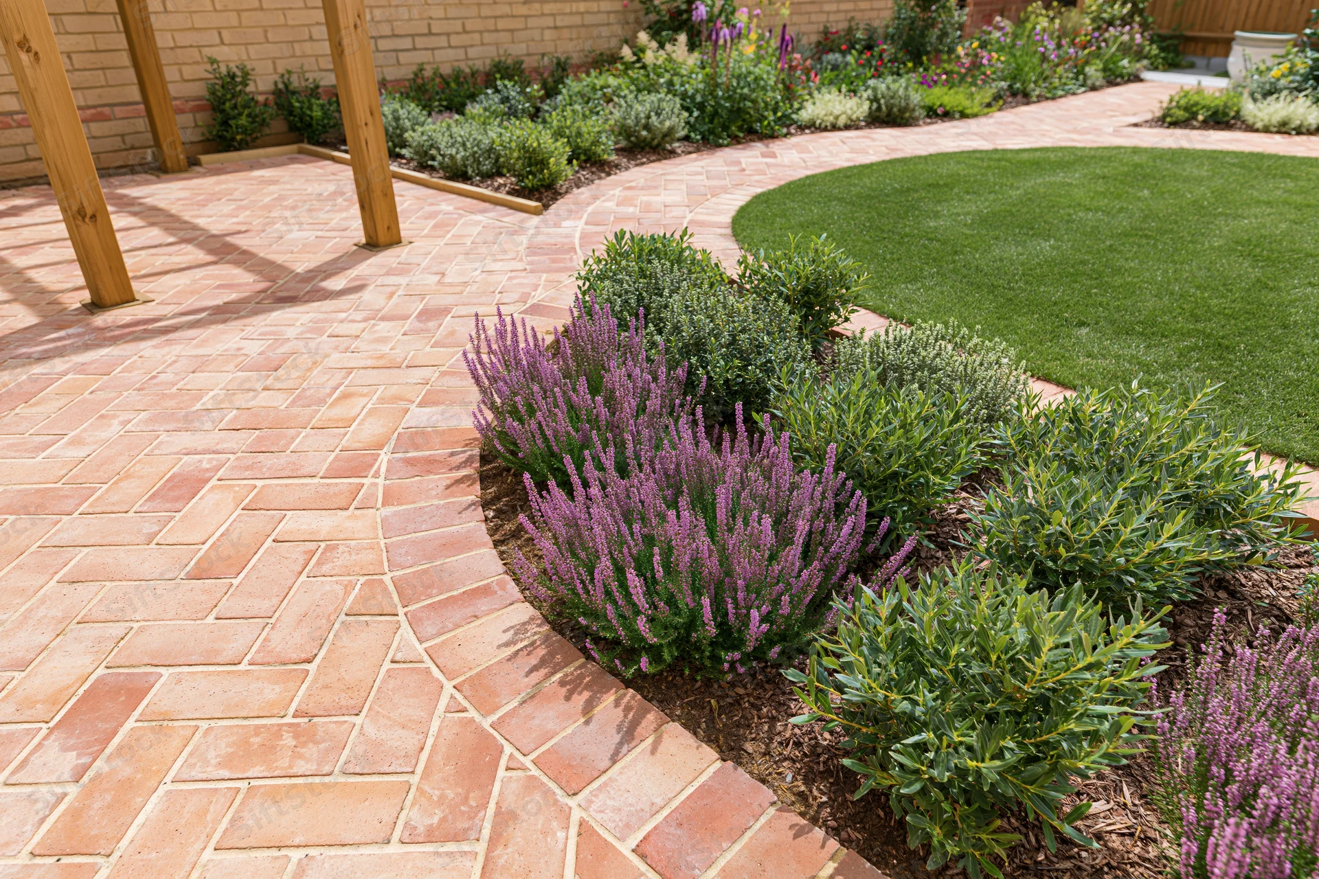 Professionally landscaped backyard garden with brick pathway curving around flowerbeds and lawn