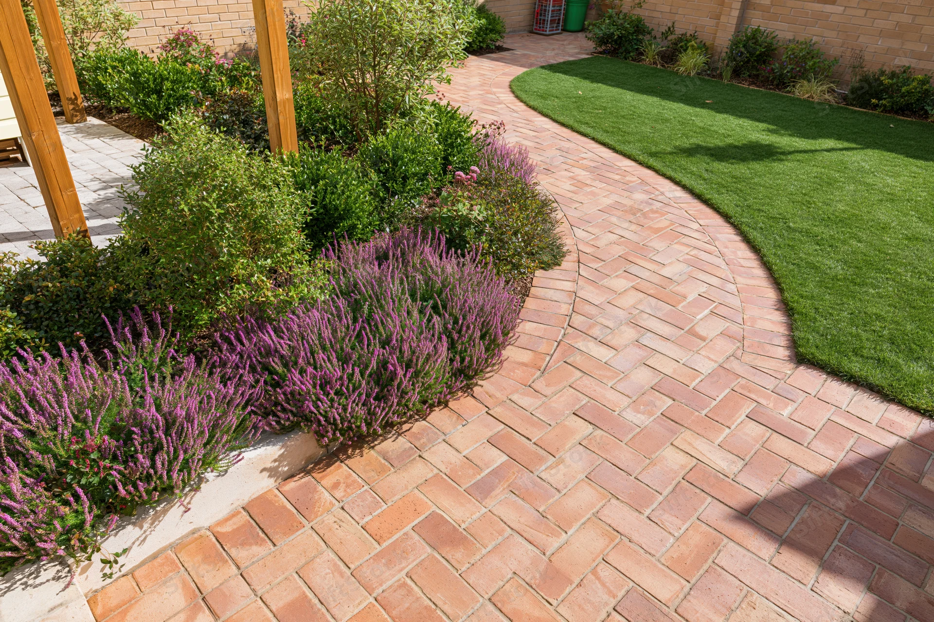 Curved brick pathway winding through landscaped garden with lavender and shrubs beside green lawn