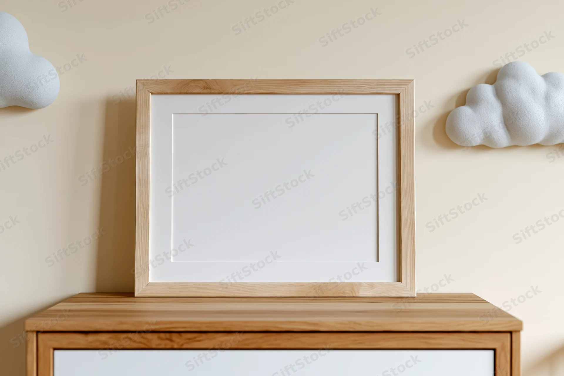 Empty light wood picture frame with white mat leaning against a dresser in a minimalist room with cloud decorations on the wall