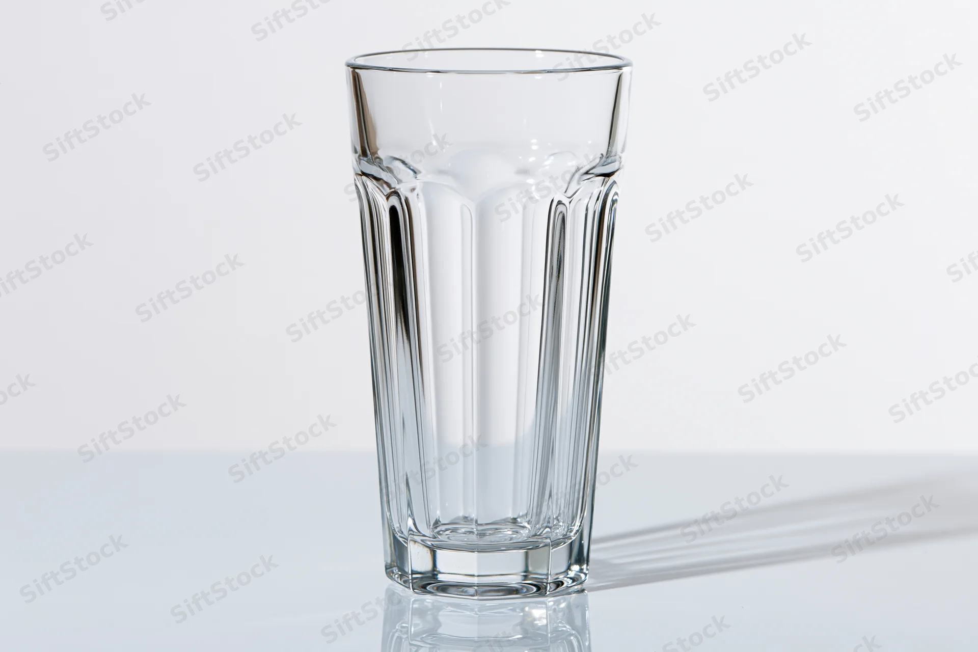 Empty tall faceted drinking glass standing upright on a white reflective surface