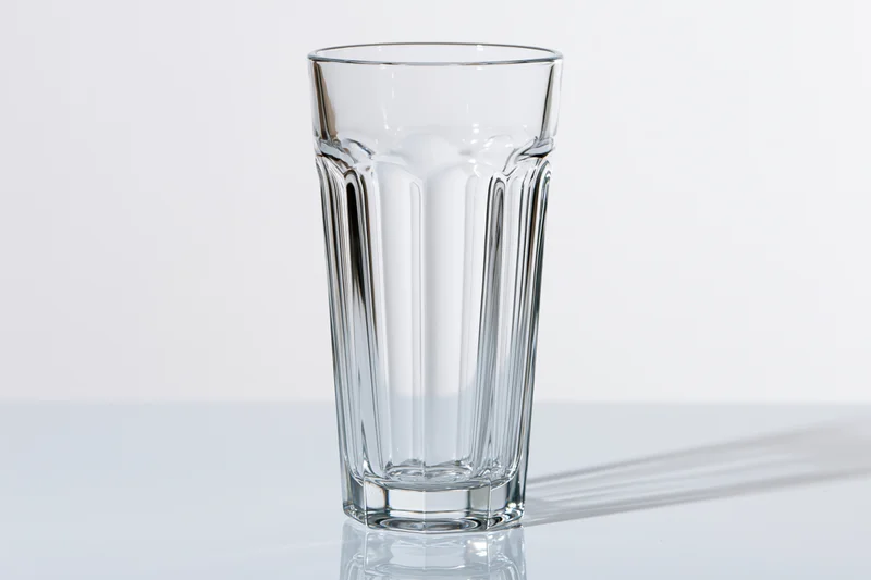 Empty tall faceted drinking glass standing upright on a white reflective surface