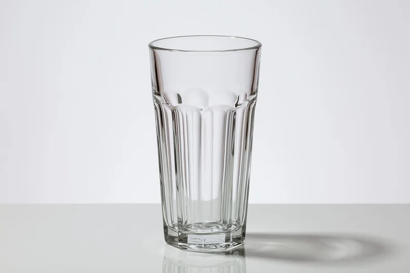 Empty tall faceted drinking glass standing upright on a white reflective surface