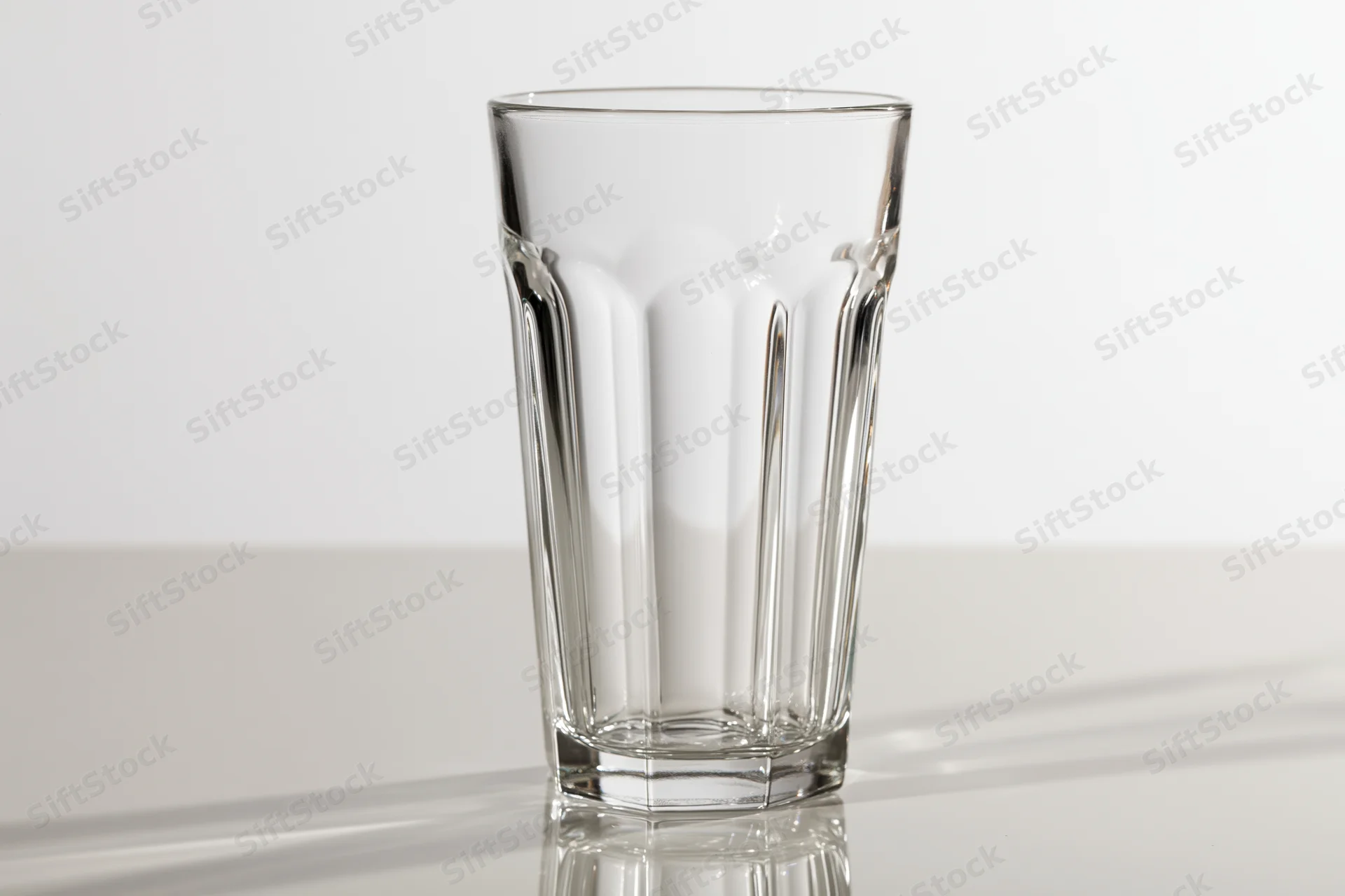 Empty tall faceted drinking glass standing upright on a clean reflective surface