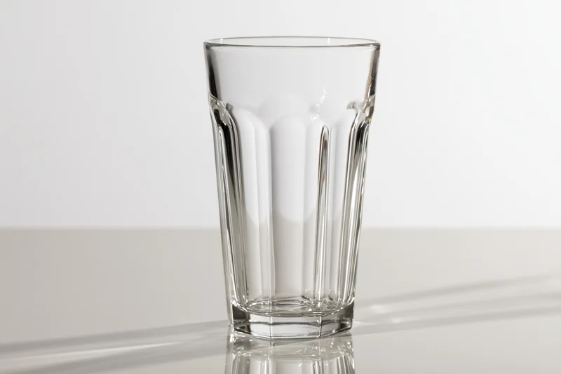 Empty tall faceted drinking glass standing upright on a clean reflective surface