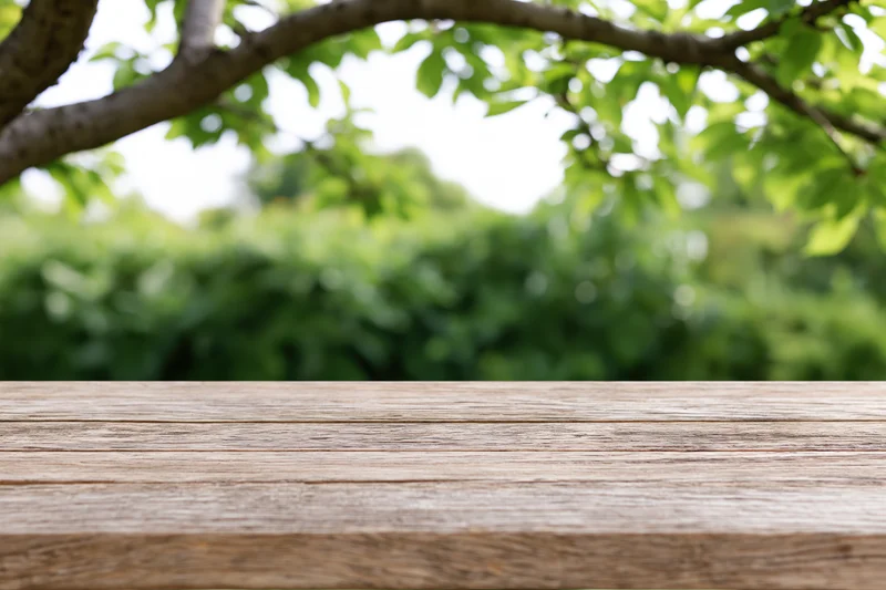 Weathered wooden table surface in front of blurred green foliage outdoors