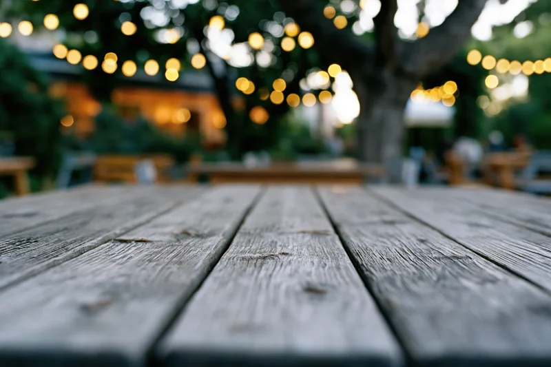 Weathered wooden table in sharp focus with blurred string lights and trees in background