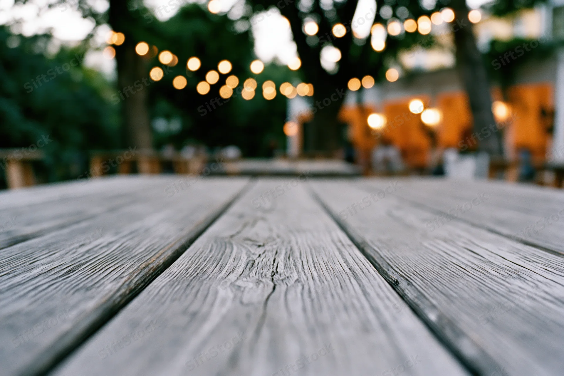 Weathered wooden deck surface in sharp focus with blurred string lights and trees in background