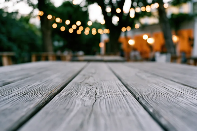Weathered wooden deck surface in sharp focus with blurred string lights and trees in background