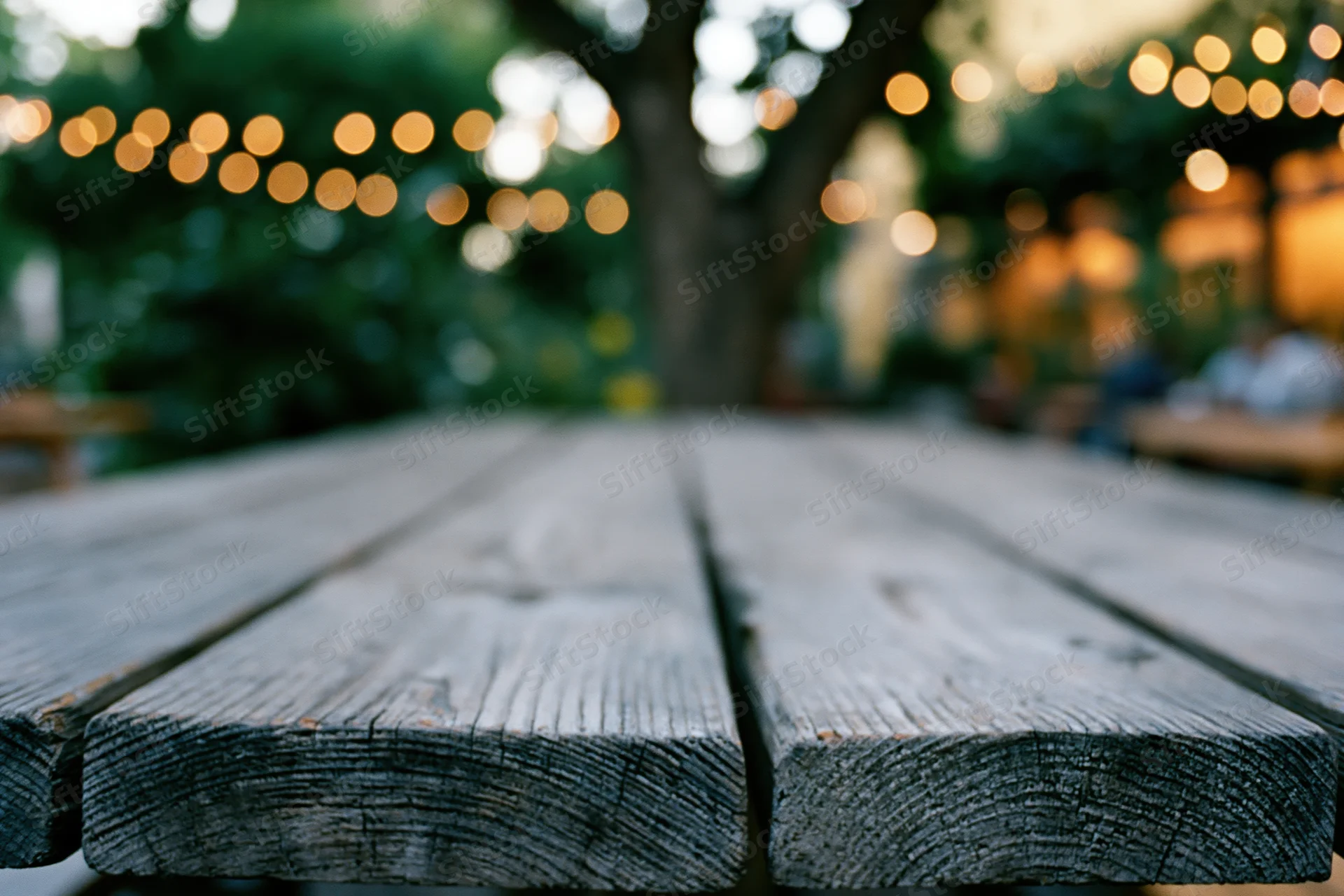 Weathered wooden table surface in sharp focus with blurred garden and string lights in background