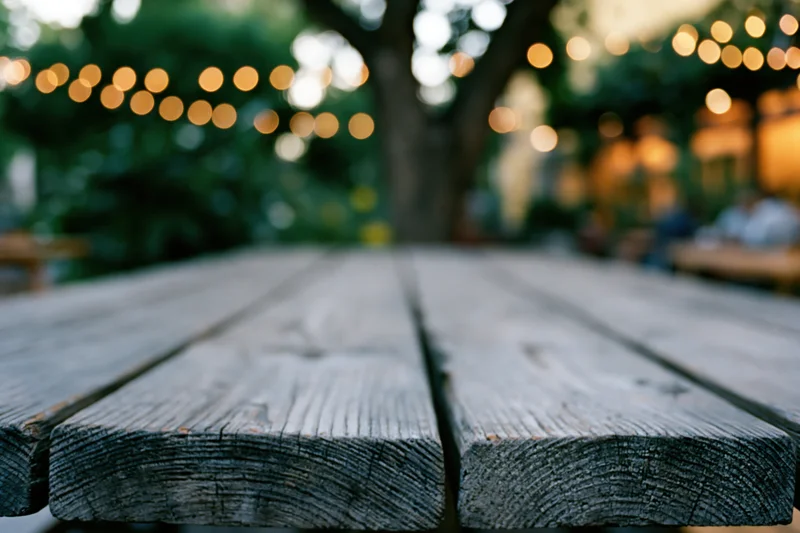 Weathered wooden table surface in sharp focus with blurred garden and string lights in background