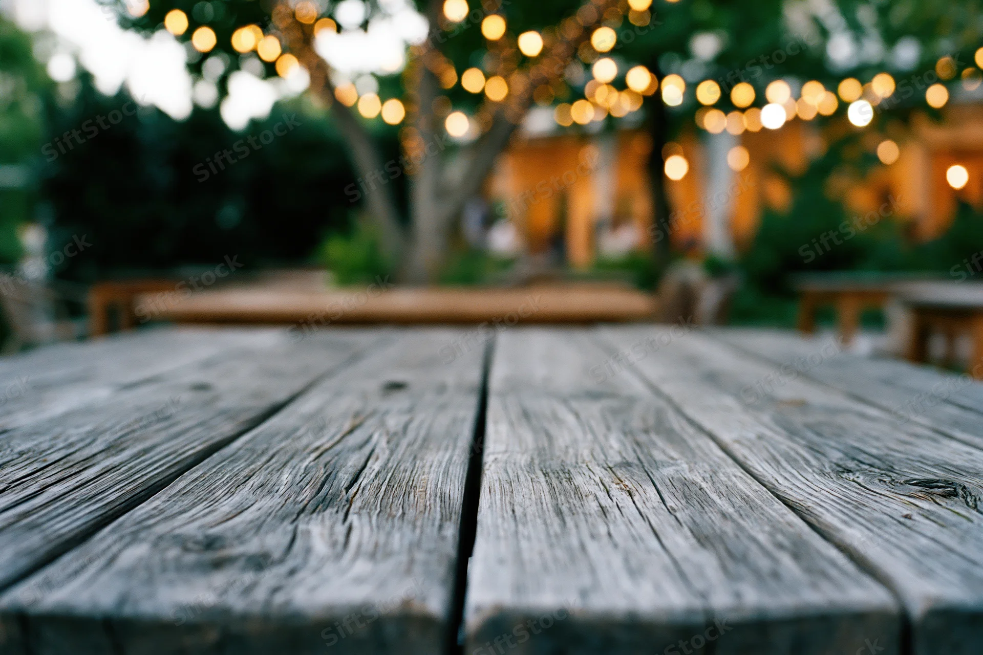 Weathered wooden table surface in sharp focus with blurred string lights and trees in background