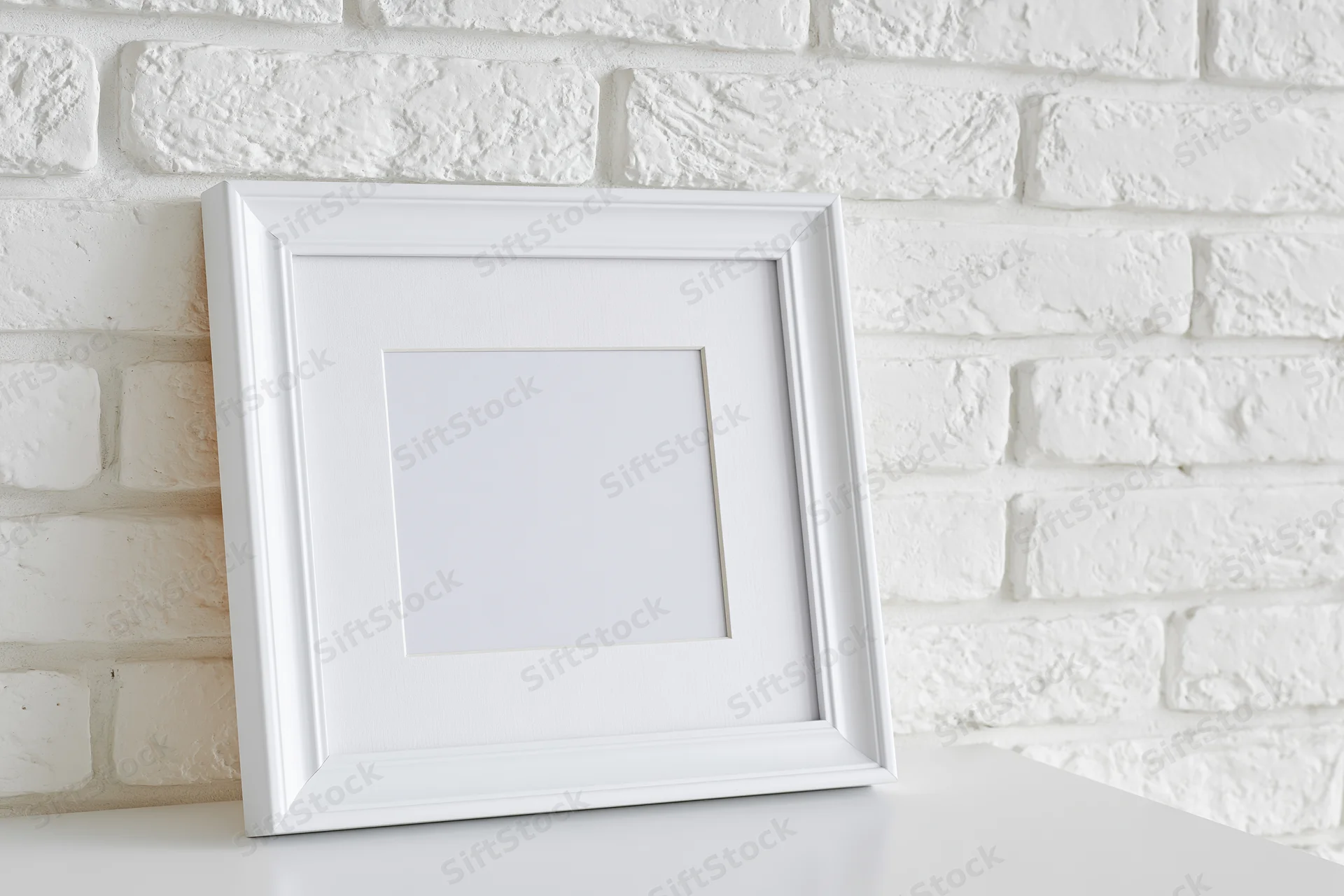 White portrait picture frame with mat insert leaning against textured brick wall on smooth white surface