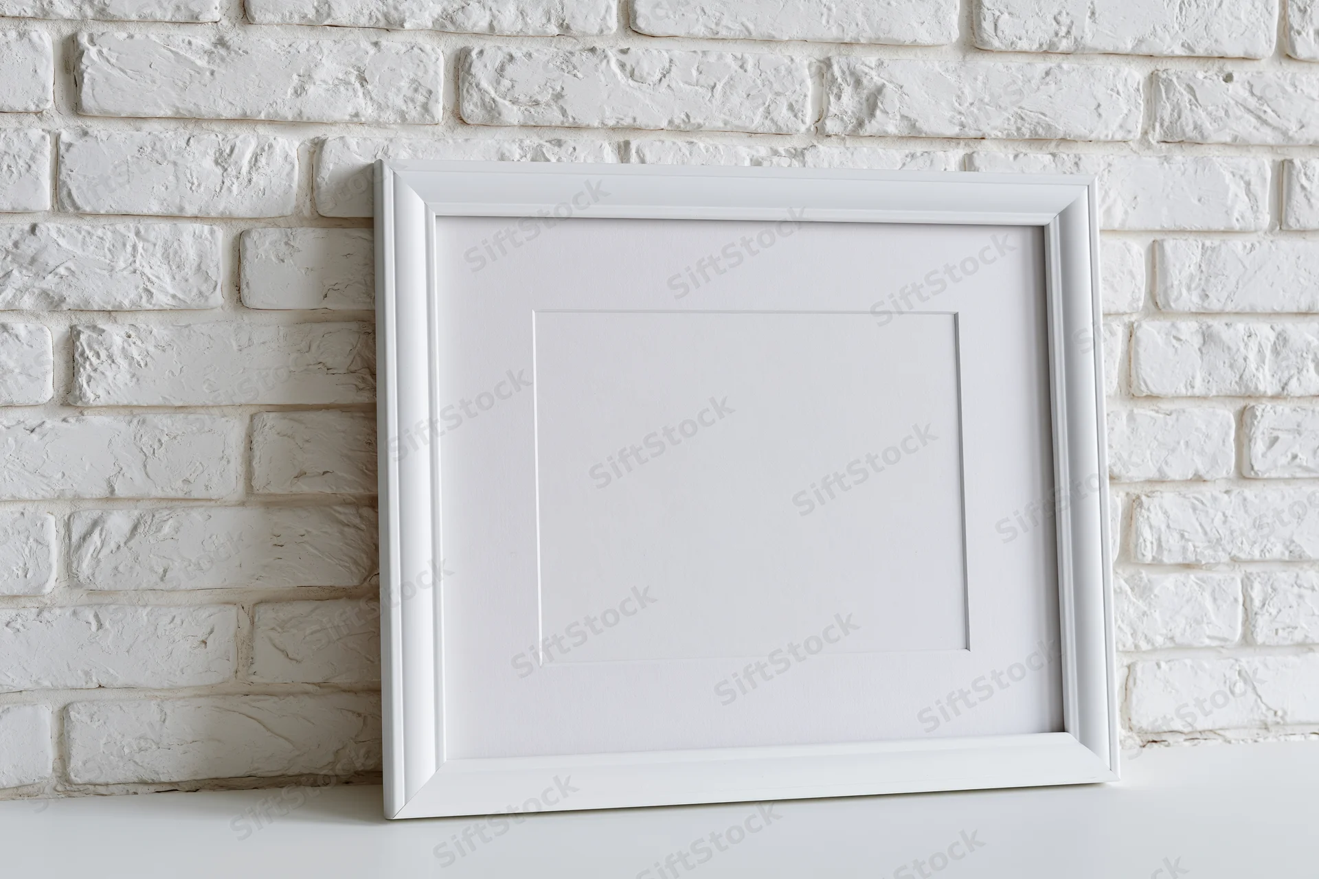 White picture frame with mat insert leaning against white brick wall on shelf