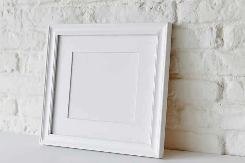 White empty picture frame with mat insert leaning against brick wall on shelf